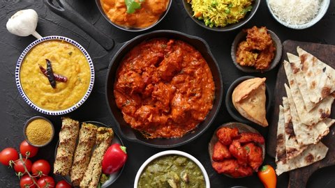 Assortment of various kinds of Indian cousine on dark rusty table. Chicken Tikka Masala, Butter, Nilgiri, Daal Tarka. Served with fried rice, naan bread and spices.