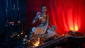 Beautiful young indian woman in traditional Sari clothing with Oriental Jewelry with a bell, and the Sitar. Indian woman Playing night Raga the Sitar, Eastern Music. Musical Candlelight Party in India