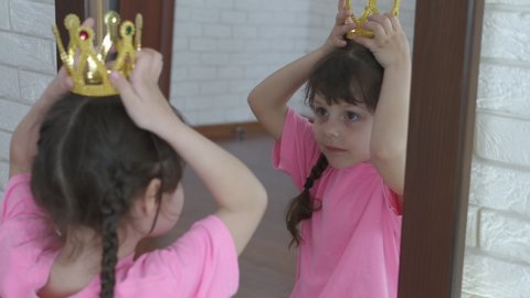 Crowned princess. Kid princess with a gold crown looks in the mirror and corrects the crown on her head.