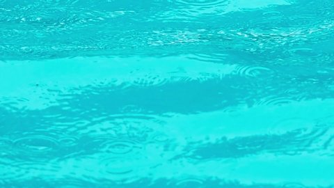 Heavy raining droplets hitting on the surface of swimming pool and water expanding ripple effect background.