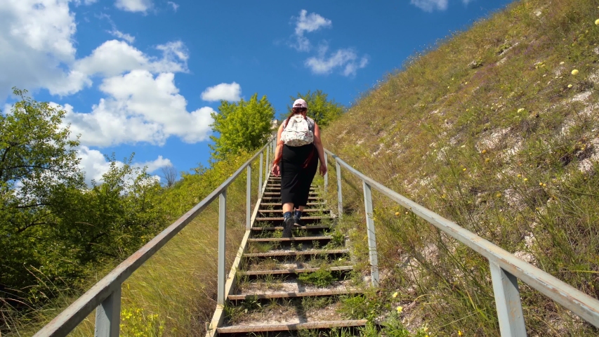 Young girl tourist climbs or goes up large steel staircase on mountain hill, summer travel adventure concept.