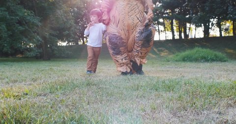 Dad and son playing at the park. Father wearing a trex dinosaur costume