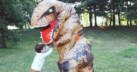 Dad and son playing at the park. Father wearing a trex dinosaur costume