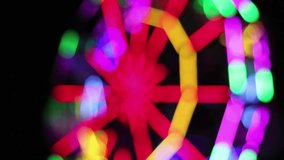 Blurred Ferris Wheel with colorful lighting decoration rotates slowly at night fun fair