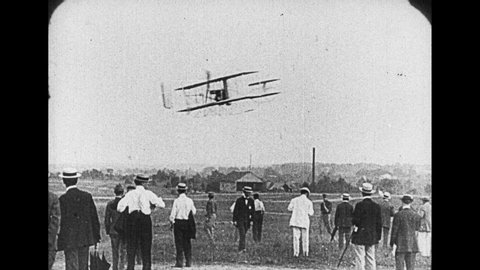 1920s: Two men sit in early Wright brothers plane. Propellers start and slingshot plane down rail to flight. Plane flies in sky then comes in for landing