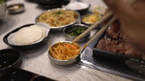 This slow motion POV video shows chopsticks grabbing banchan korean bbq food and moving it towards the viewers mouth to eat.