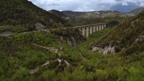 Long concrete bridges over the green hilly valley on the cloudy sky background in Basilicata region in Italy. There is a moving car on the nearest of them. Aerial video recording with forward motion.