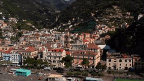 Wonderful sunny cityscape of Minori town on Amalfi Coast in Italy. There is Basilica of Santa Trofimena with a bell tower, many multicolored houses on the green hills background. Video recording.