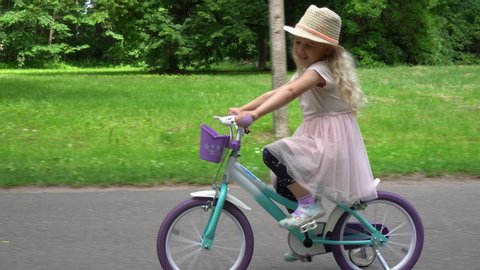 Little Adorable Caucasian Girl with Hat Rides On Bicycle In City Park. Stabilizer Gimbal movement motion shot
