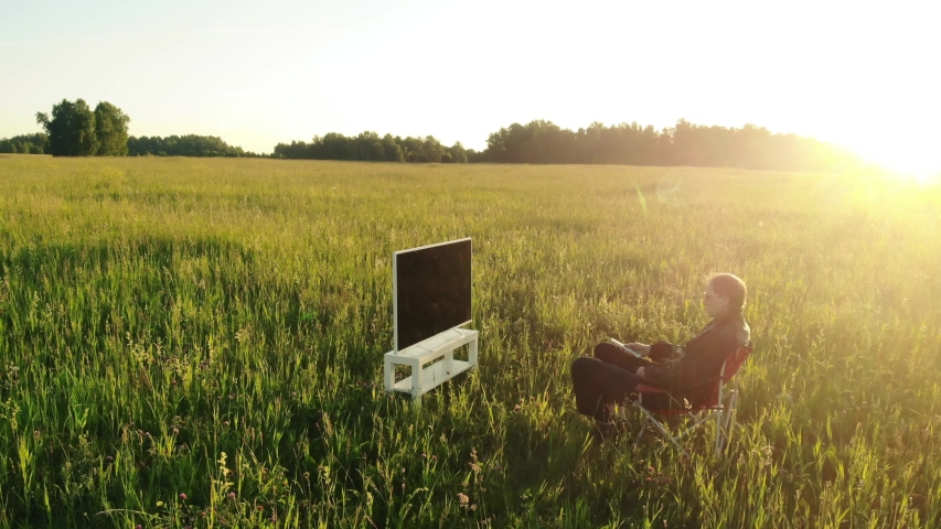 Man sits in front of the TV on the lawn crane shot.