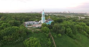 4K quality aerial video scenic view of beautiful light blue church overlooking green park, distant city and hills in Krylatskoye area on quiet cloudy afternoon near Moscow River in Moscow, Russia