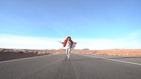Girl running on empty highway road with USA flag in the air, travel America concept; Young woman on road running slow motion  