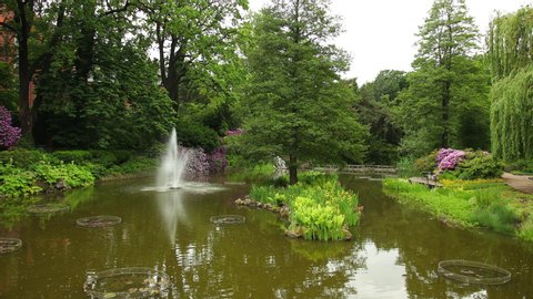 Beautiful panorama of flowers, trees and bushes in botanical garden in Wroclaw, Poland. The fountain throws water out of pond upwards. Purple, yellow, green, white colorful colors of a wonderful park