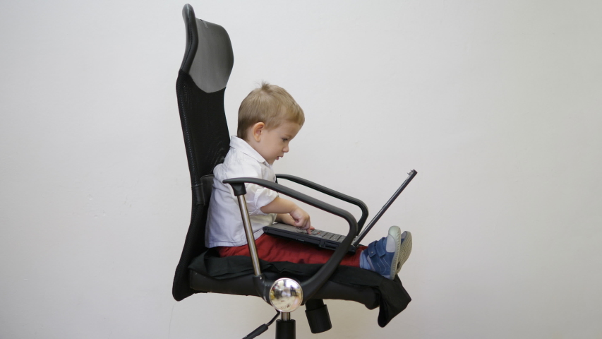 Portrait of little child working at laptop on business chair, early job