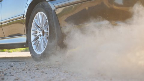 Detail view on wheel of powerful car starting movement and slipping on asphalt road. Small stones and dust flying out from under tire of auto. Vehicle beginning motion. Concept of burnout. Slow motion