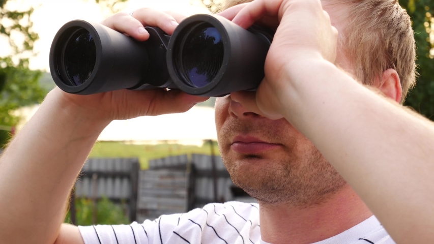 Handsome man looks through binoculars then puts them down and looks thoughtfully into the distance. Closeup