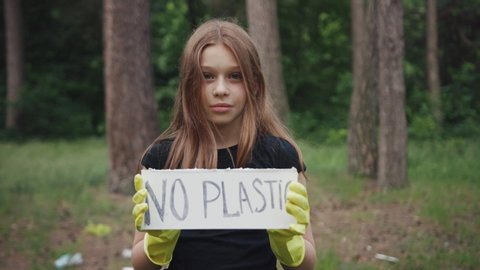 Save the planet for future. Portrait of a sweet teen girl showing a sign protesting against plastic pollution in the forest. No plastic concept. Eco-friendly environment.
