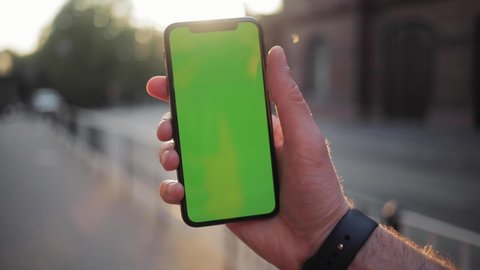 NEW YORK - April 5, 2018: Man hand using phone with horizontal green screen smart mobile view blurred background chromakey swapping flipping display touchscreen sunset sunshine business internet touch
