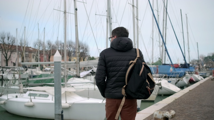 Pedestrian is walking on city quay with moored boats in Rimini, Italy
