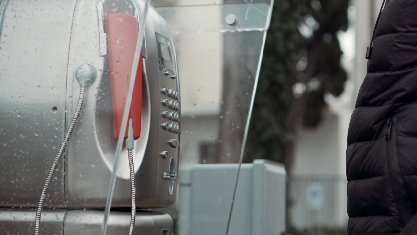 Man is calling by public telephone on street in city, holding handset