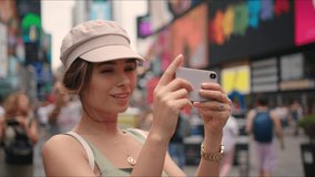 Pretty girl looks around and shoots video on phone at Time Square.