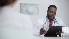 positive african american doctor talking with colleague while looking at clipboard with diagnosis