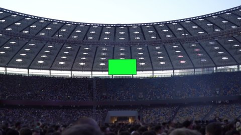 Crowd of people stand in an open stadium with Big TV Green Screen or Chroma key background