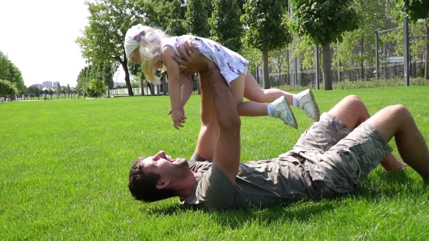 Father with baby daughter playing in the park on the grass.