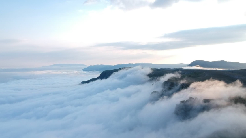 drone smoothly flies down over the cliffs of the tops of the mountains through which heavy white clouds are trying to climb ridge retains fog