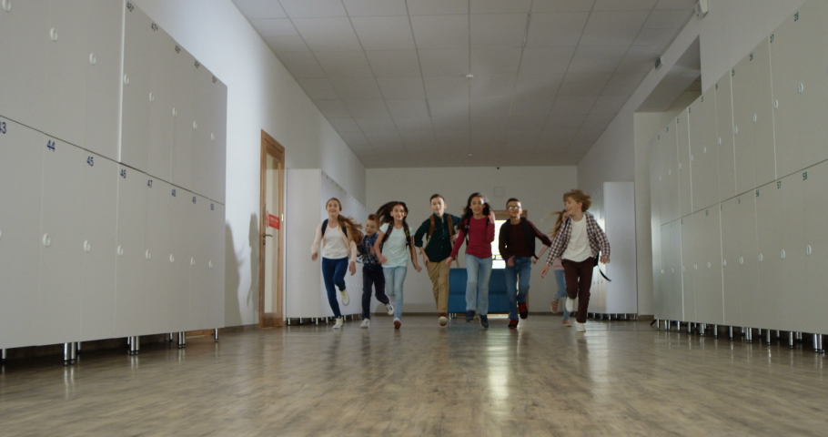 Joyful Caucasian pupils, teens girls and boys with schoolbegs, running happily the long school corridor after lessons or during the break.
