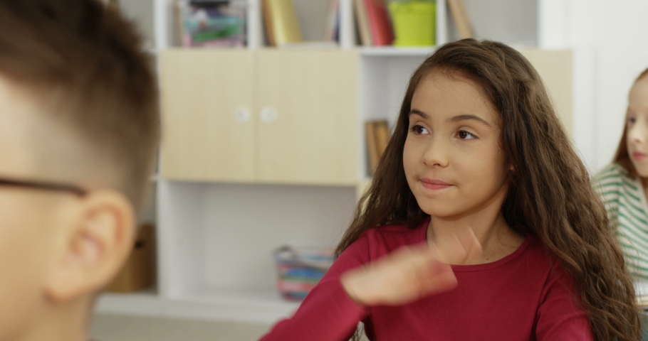 Close up of the nice Caucasian teen small schoolgirl answering the teacher question with rised hand in the school at the lesson.