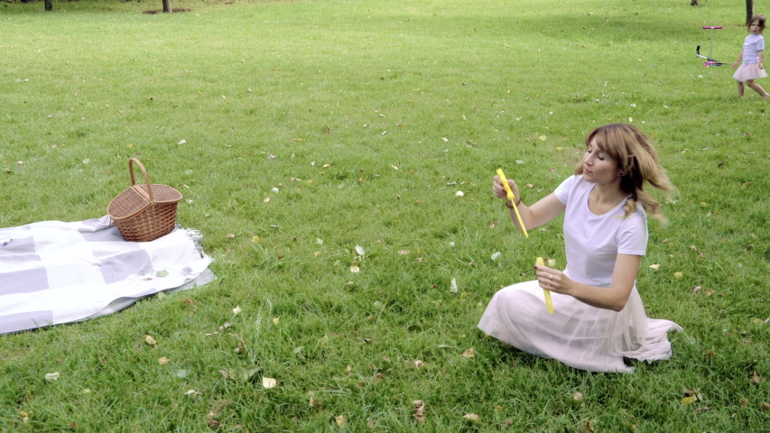 Happy mother and her two kids playing together, blowing and catching soap bubbles outdoors