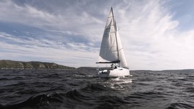 Original high waves and blue sky with clouds. The yacht with white sails goes forward. On the horizon a mountain shore. Clean sea air. Atmospheric video.