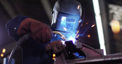 4K Female metalworker in industrial workshop lifting up mask to check her work. Slow motion.