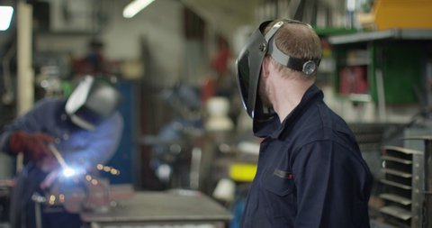 4K Mechanic in garage workshop lifting his welding visor & looking at camera. Slow motion.