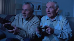 Emotional elderly male friends holding joysticks and playing video game, fun