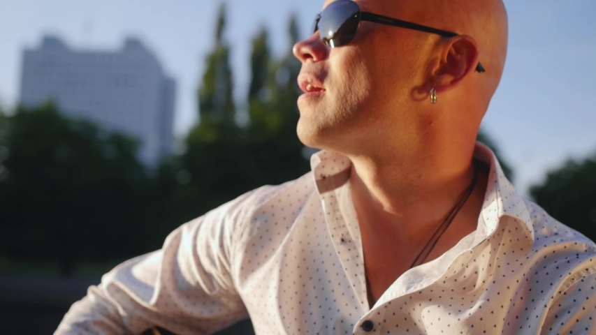 Man plays guitar and sings against the lake. Guitarist touching guitar strings. Close up shot.