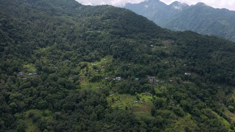 Sikkim, India - 06 10 2019: SIKKIM, INDIA, JUNE 10 - Aerial, tilt down, drone shot, towards a house and a green garden, in a small town, on a mountain wall, surrounded by Indian forest, on a partly su