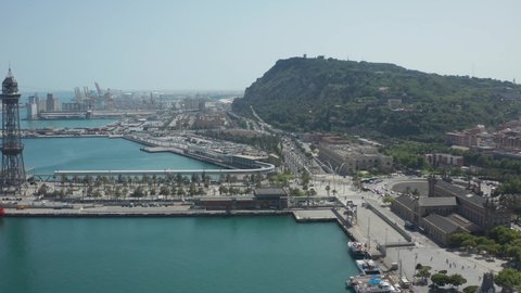 Drone flight over port part of Barcelona city with mountain Montjuic aside. Aerial shot of city traffic, green Montjuic, industrial harbors of large commercial port in Barcelona, Catalonia, Spain