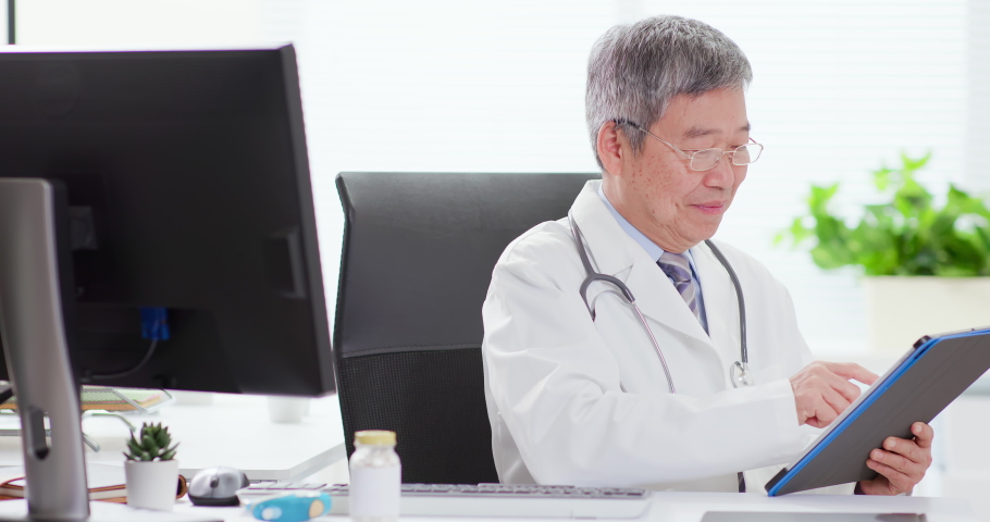 Senior male doctor smile to you after using tablet pc