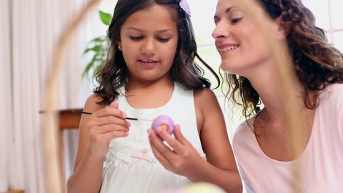 Mother and daughter painting easter eggs at home in kitchen