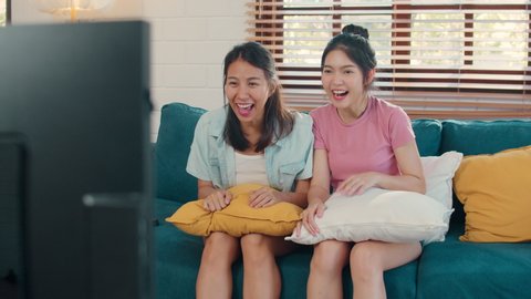 Asian Lesbian lgbtq women couple watching TV at home, Young Asia lover female feeling happy fun laugh cheer soccer football together while lying sofa in living room at home concept.