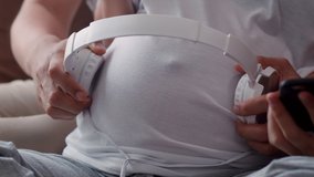 Young Asian Pregnant couple using phone and headphone play music for baby in belly. Mom and Dad feeling happy smiling peaceful while take care child lying on sofa in living room at home concept. - Powered by Shutterstock - Get 15% off with code: PIKWIZARD15