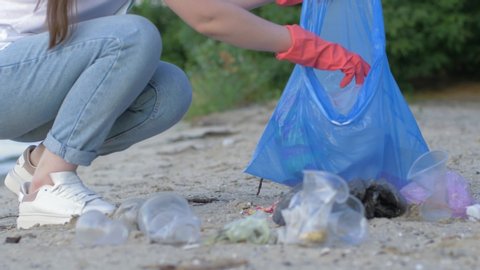 care nature ecology, volunteer girl in rubber gloves collects plastic rubbish in garbage bag while cleaning waterfront close up