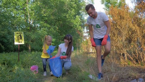young volunteer male and female with child girl cares about ecology environmental and collect plastic dregs in garbage bag during cleaning from pollution outdoors