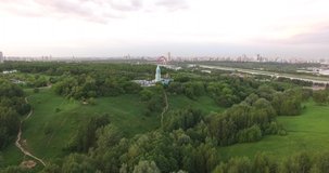 4K quality aerial video scenic view of beautiful light blue church overlooking green park, distant city and steep hills on quiet cloudy afternoon on the outskirts of large city