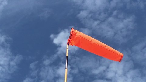 Orange windsock in moderate wind on pole against clear blue sky on sunny day