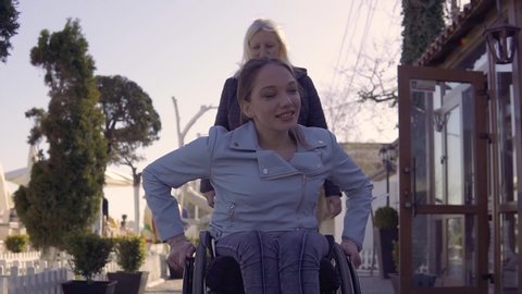 Family leisure. Young disabled woman in wheelchair with her mother walking near the sea, speaking and having fun Vídeo Stock
