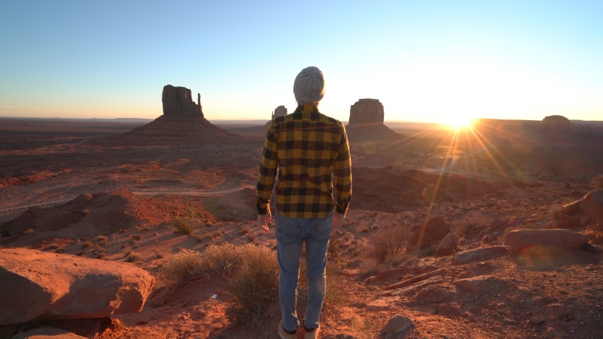 Man rising arms at sunrise in the morning embracing travel in USA at Monument Valley; Travel young man enjoying nature and wilderness