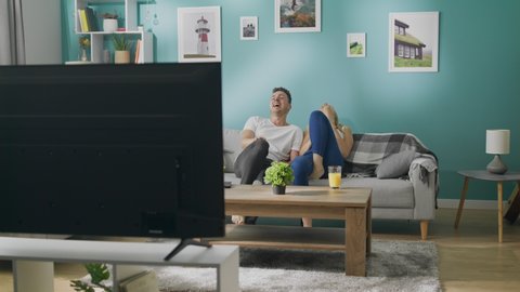Happy young couple watching tv on couch in cozy living room